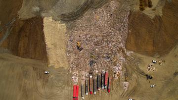 Drone overhead, trash haulers unloading waste at the landfill