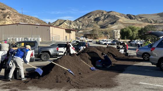 OC Residents using shovels to pick up compost on a tall pile at a landfill site