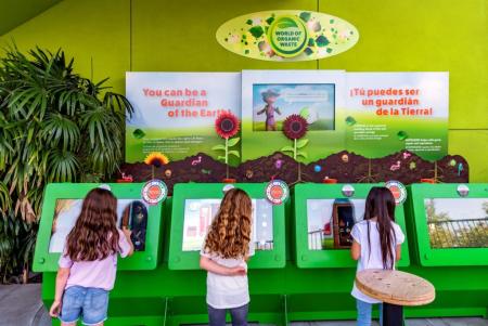 Three children interact with touchscreen exhibits at the World of Organic Waste display, learning about composting and how food scraps become healthy soil.